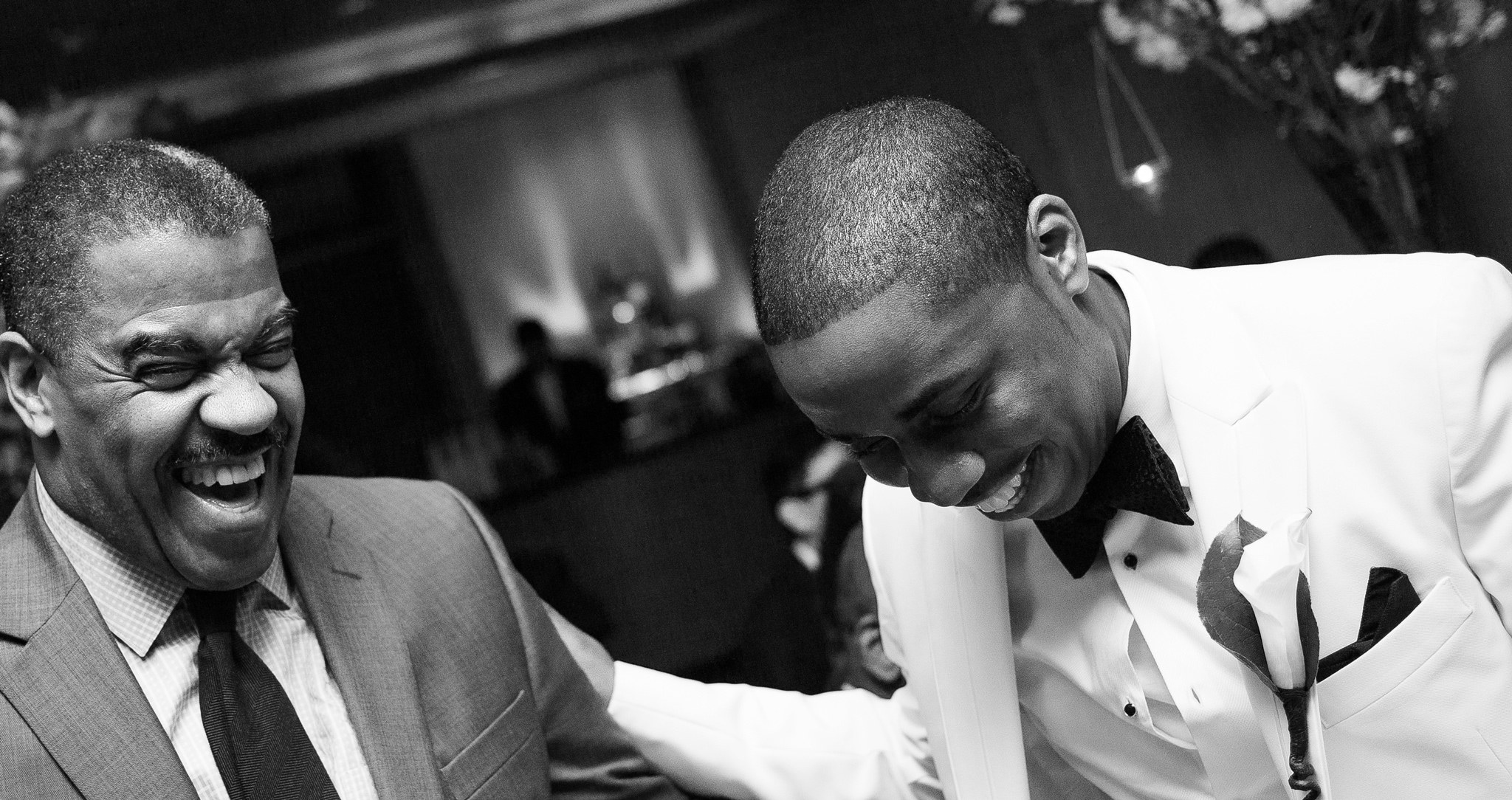 Two men in suits share a laugh at the reception, in black and white