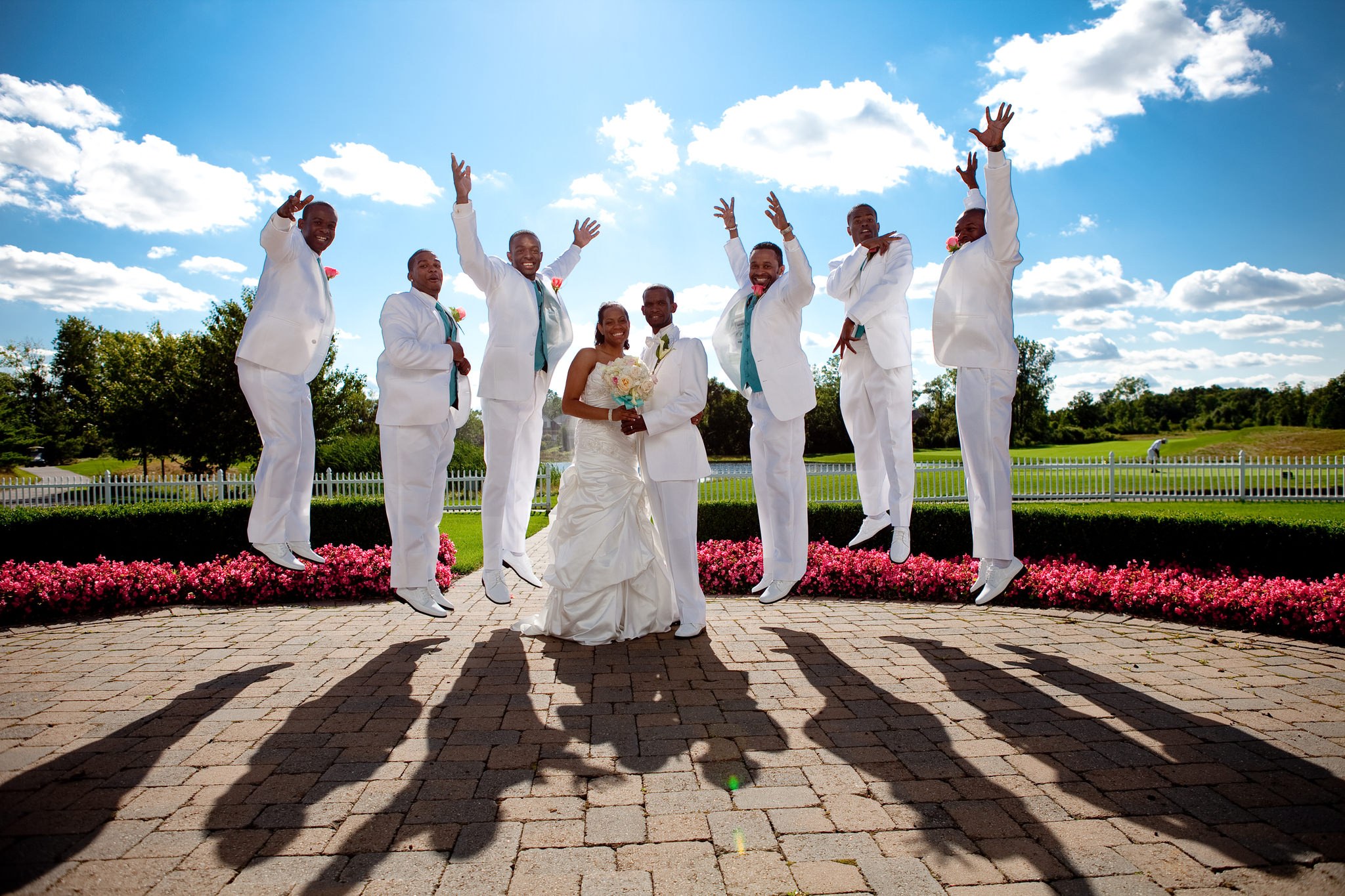 The wedding party leaps in the air together on a sunny lawn