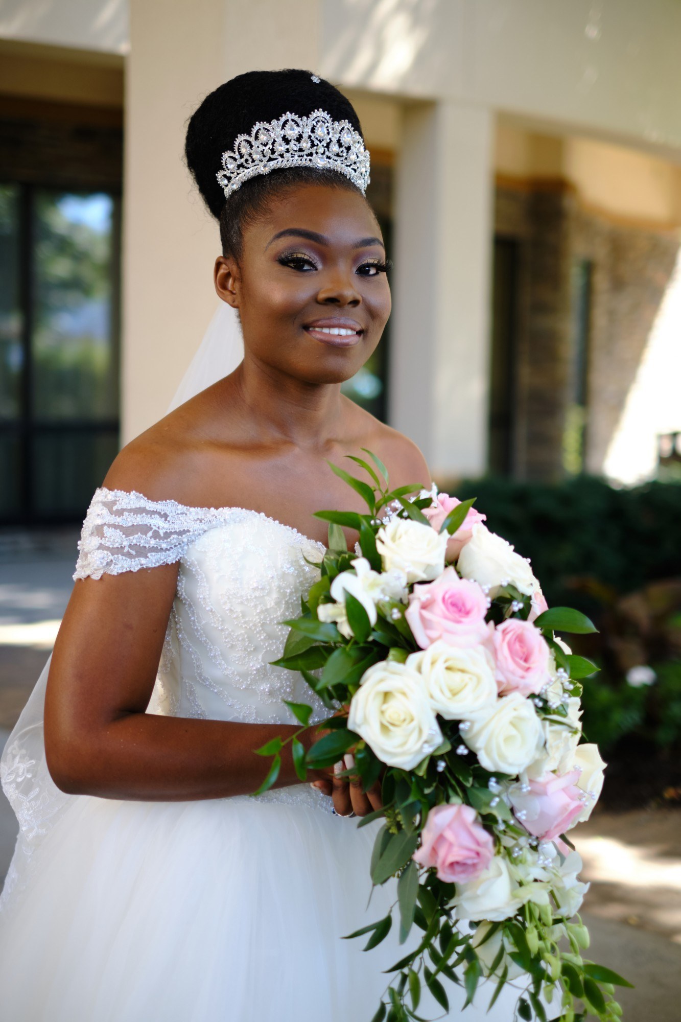 A bride in a tiara holds a cascade of white and pink roses